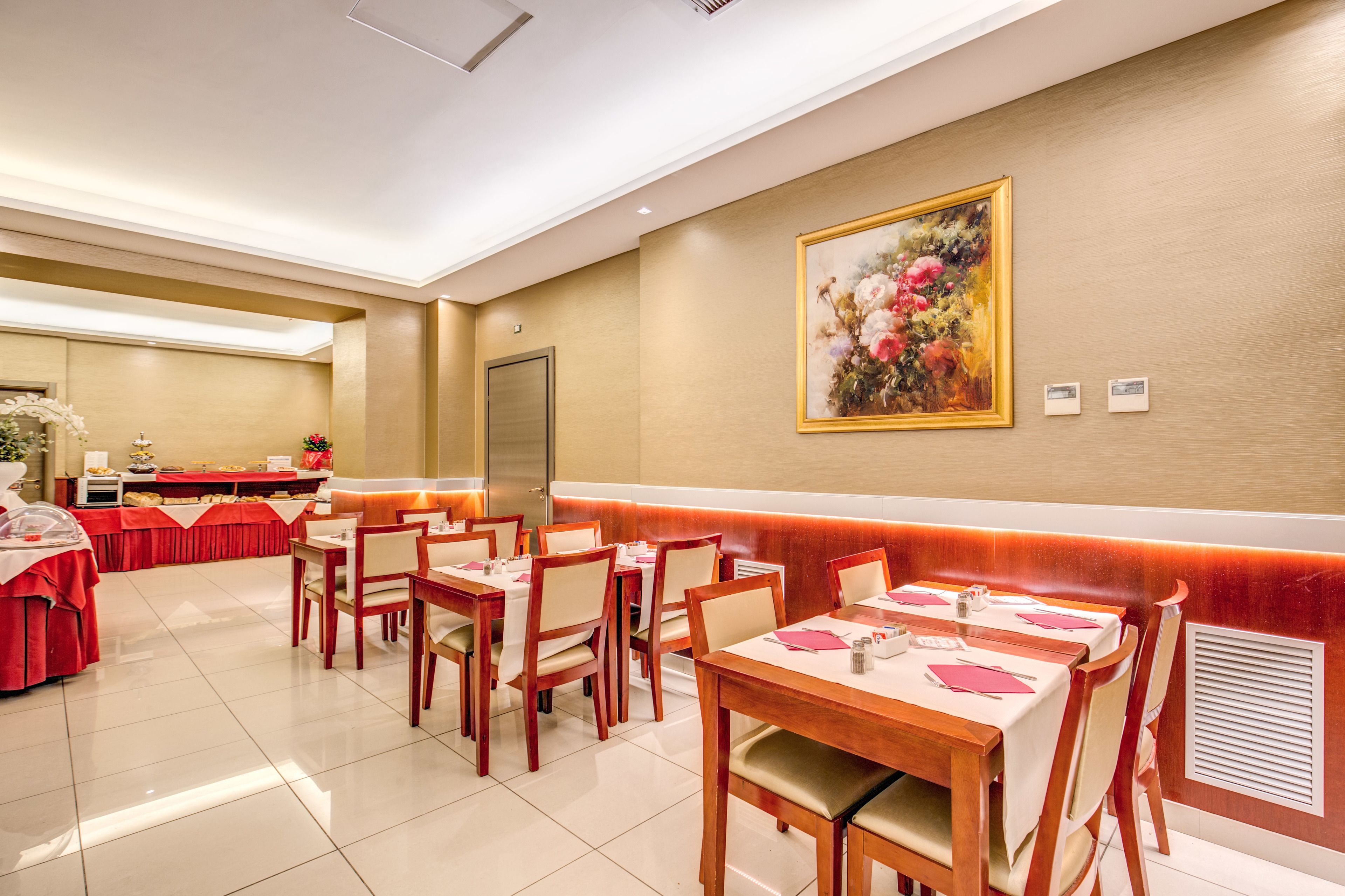 A dining area with tables set for service, a buffet line, and a large floral painting on the wall.