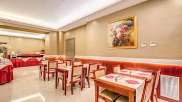 A dining area with tables set for service, a buffet line, and a large floral painting on the wall.