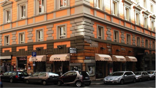 Un edificio de varios pisos con entrada en esquina, que cuenta con una tienda boutique llamada 'nina' en la planta baja.