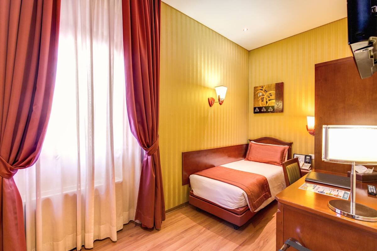 Ein Hotelzimmer mit einem Bett, einem Schreibtisch mit Lampe und einer Wandleuchte.