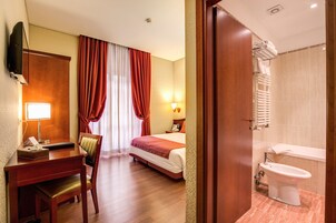 A hotel room with a desk, chair, bed, and a bathroom with a toilet and shower.