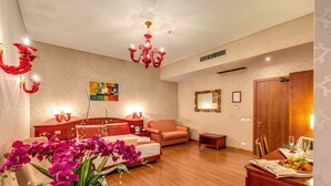 Amplia habitación de hotel con una cama grande, zona de estar, mesa de comedor con fruta y una araña.