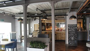 Interior de una cafetería moderna con mesas de madera, barra y cartel en una pizarra.