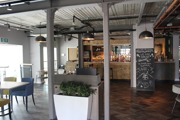 Interior de una cafetería moderna con mesas de madera, barra y cartel en una pizarra.