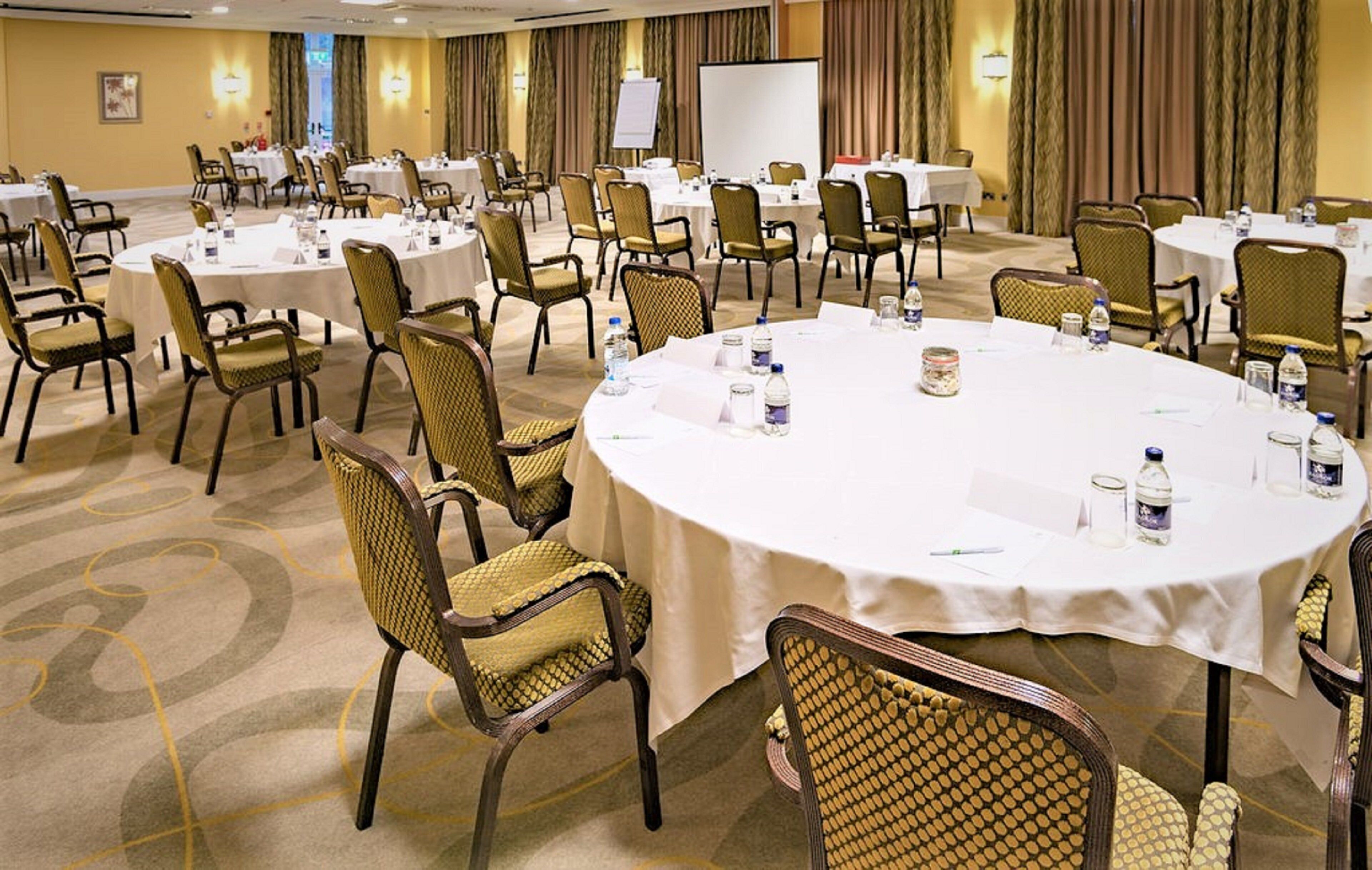 Une salle de conférence équipée de tables rondes, de chaises et d’écrans de présentation.