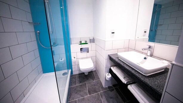 A modern bathroom with a glass shower enclosure, a white toilet, a sink with a granite countertop, and a large mirror. - Holiday Inn Kenilworth - Warwick by IHG (Kenilworth)