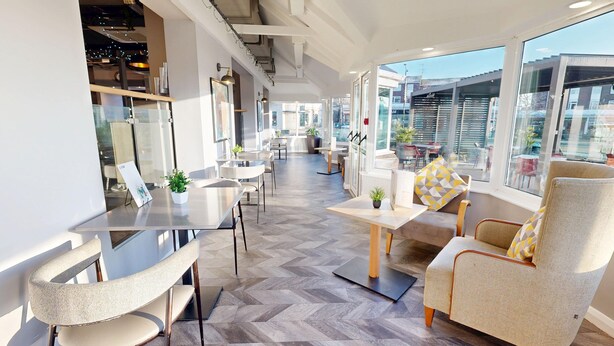 Un interior moderno con una larga mesa de comedor, asientos cómodos y grandes ventanales que ofrecen vistas de la ciudad.
