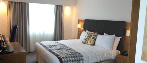 Quarto de hotel com uma cama grande, uma escrivaninha com cadeira, telefone e abajur.