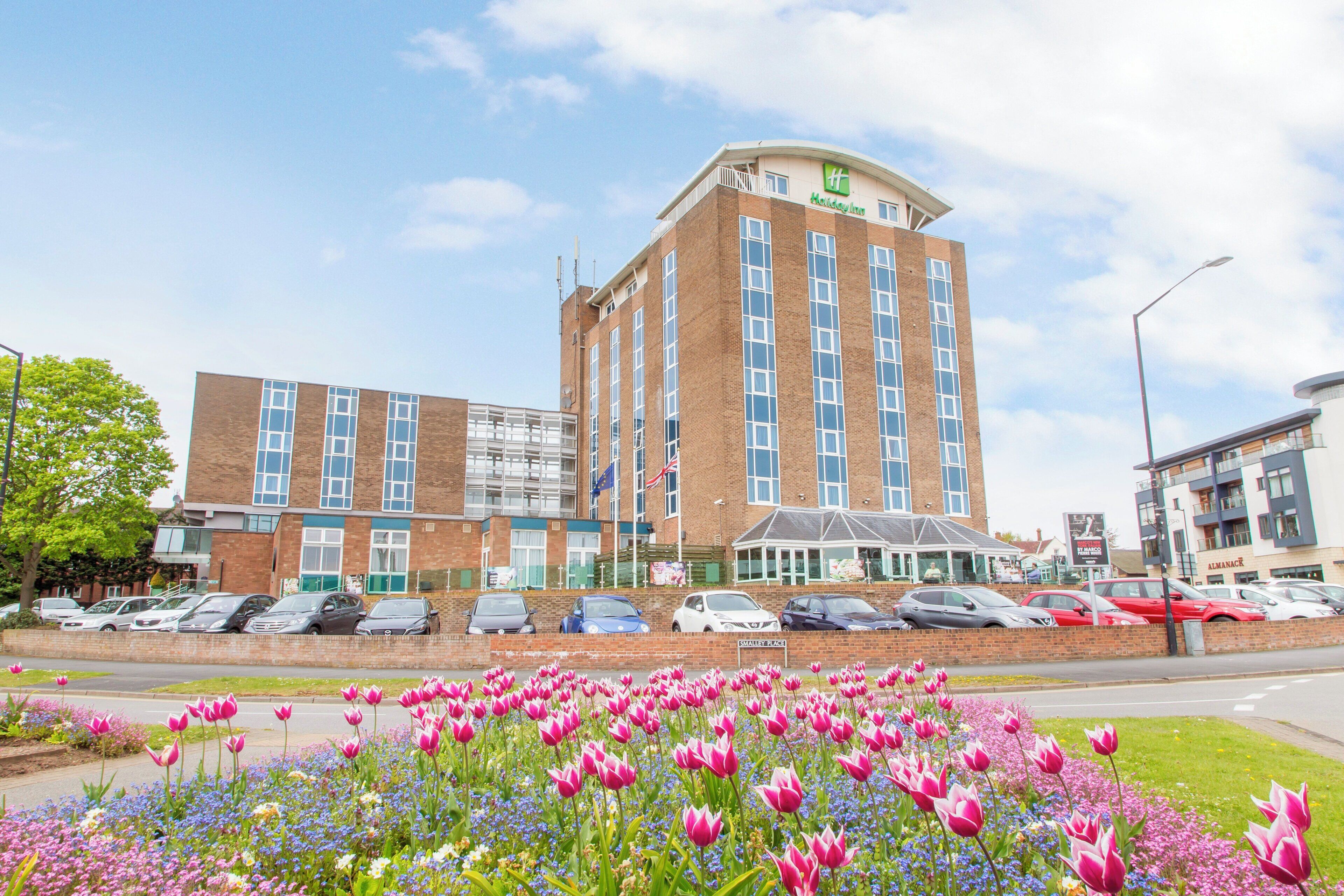 A Holiday Inn hotel with a parking lot and a flower garden in front.