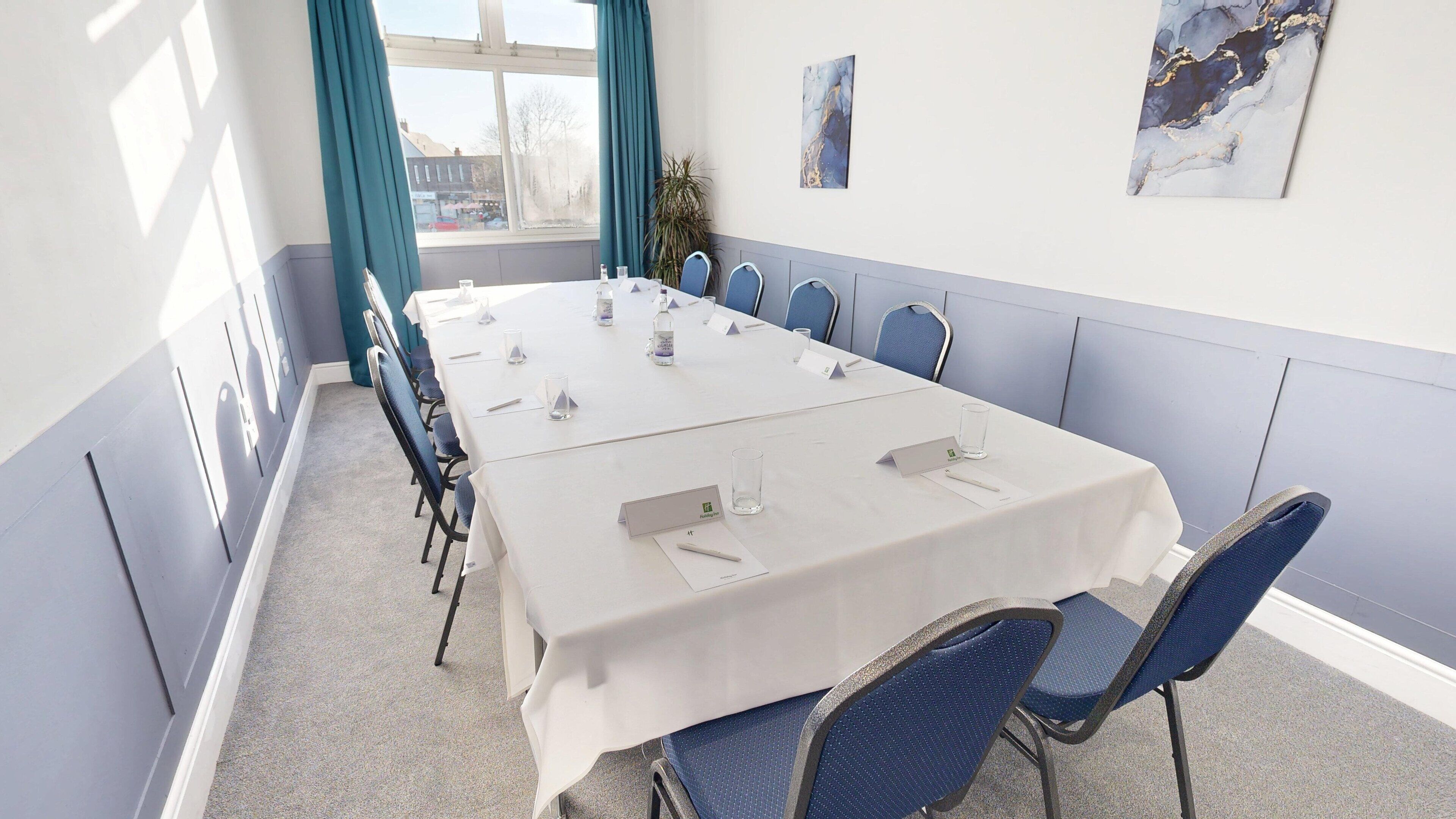 A conference room with a long table, chairs, name cards, and a window with curtains.