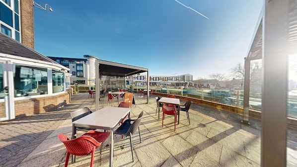 Un patio al aire libre con mesas y sillas, una zona de estar cubierta y vistas a la ciudad.