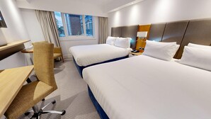 Habitación de hotel con dos camas, un escritorio, una silla, un teléfono y una ventana con cortinas.