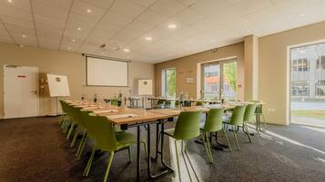 A conference room with a long table, green chairs, a projector screen, and a whiteboard.