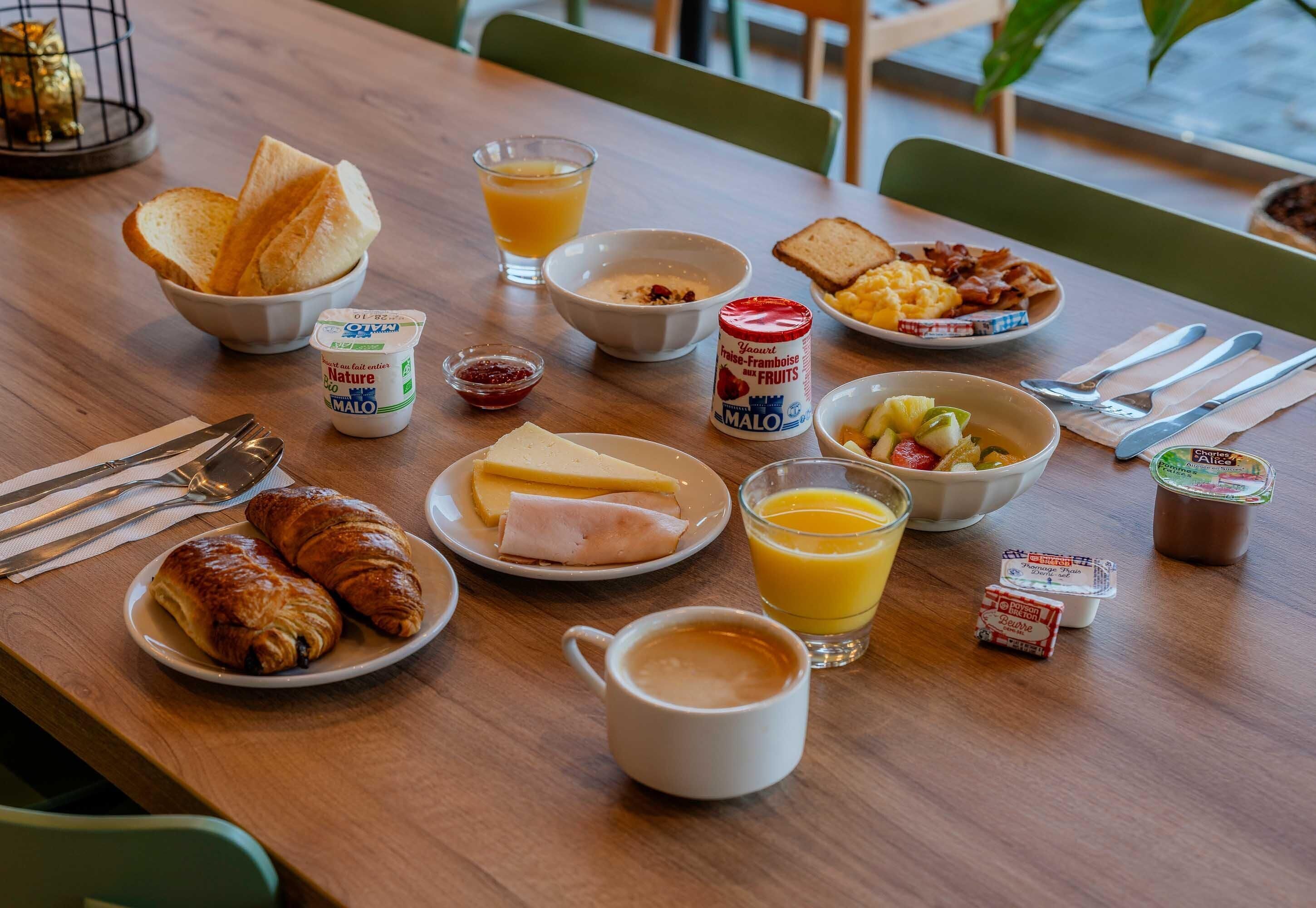 Una mesa de desayuno con croissants, tostadas, fruta, yogur y café.