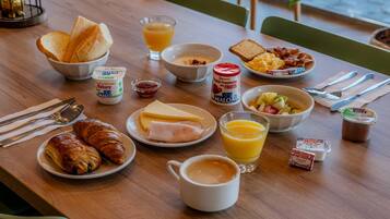 Una mesa de desayuno con croissants, tostadas, fruta, yogur y café.