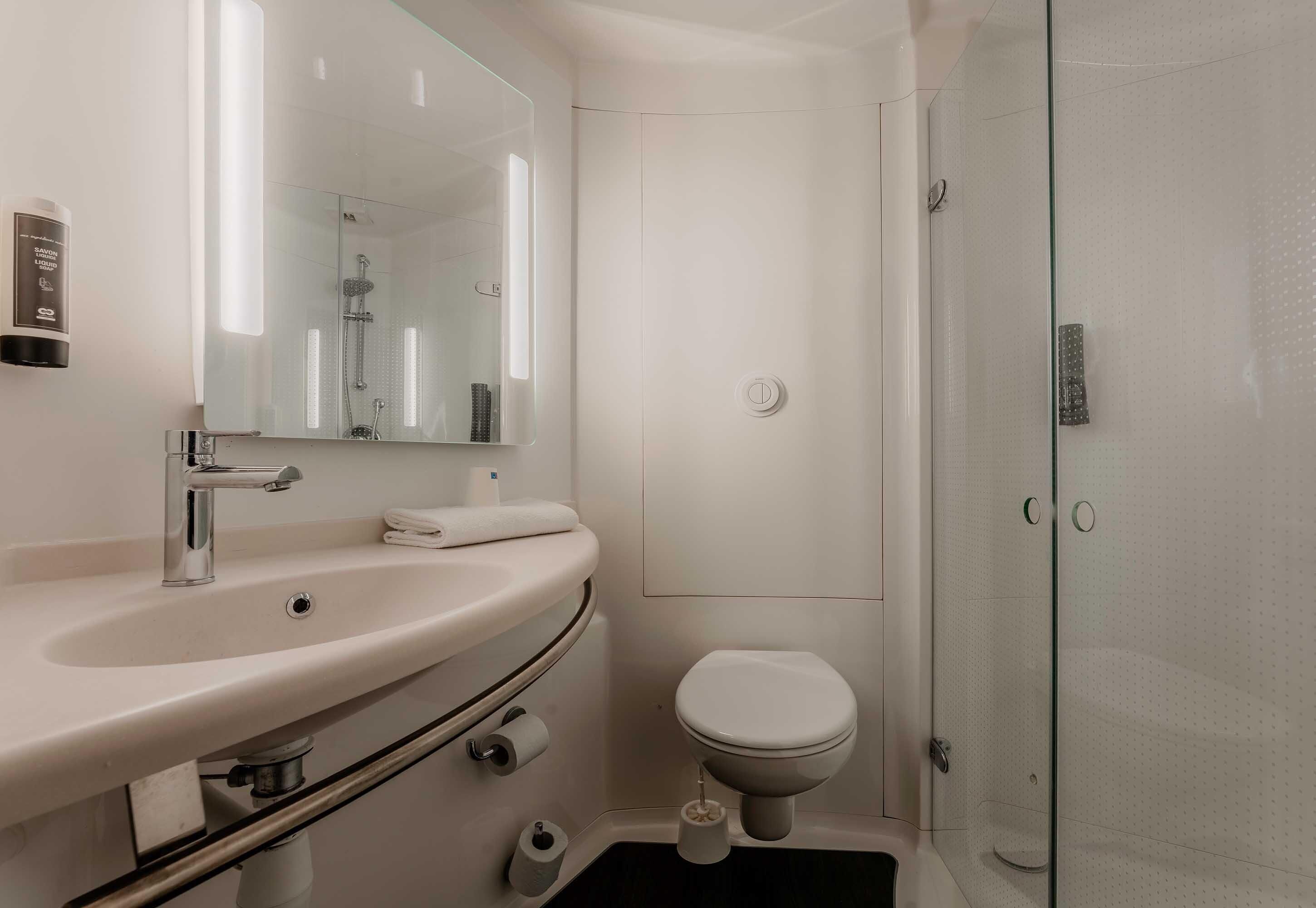 Une salle de bain moderne équipée d’un lavabo, d’un miroir, de toilettes et d’une douche à parois en verre.