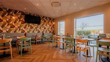 A cafe with wooden flooring, green and orange chairs, and a large window.