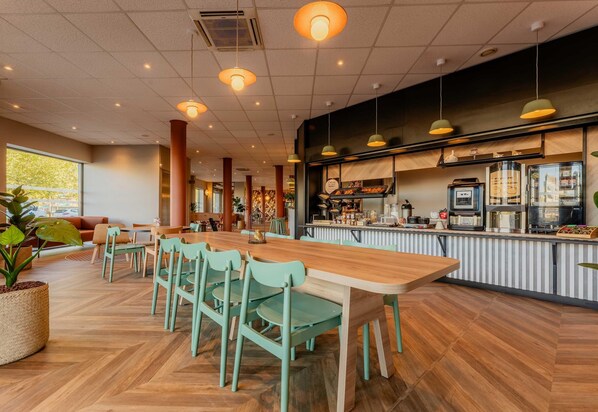 A modern cafe with a wooden table and chairs, a counter with coffee machines, and a large window.