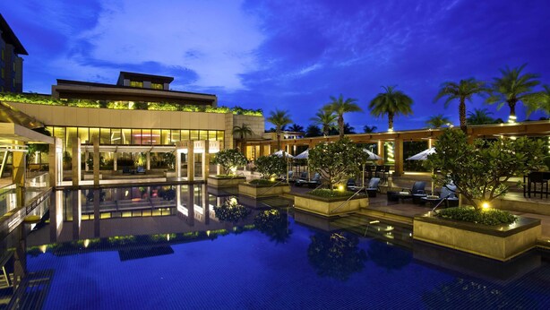 Un hotel moderno con una amplia piscina al aire libre, zonas de descanso y palmeras.