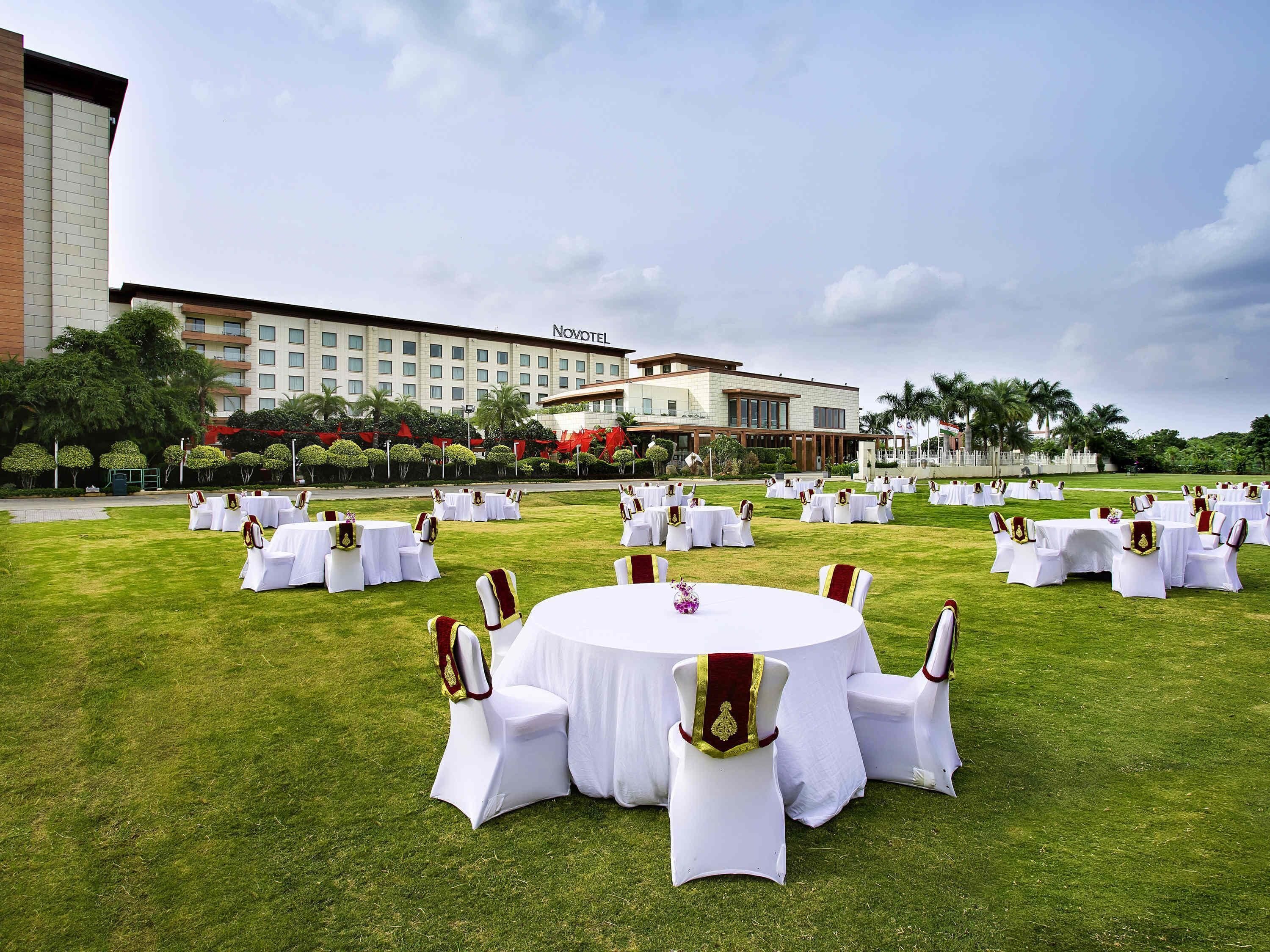 A hotel courtyard with round tables and chairs, a large building in the background, and a well-maintained lawn.