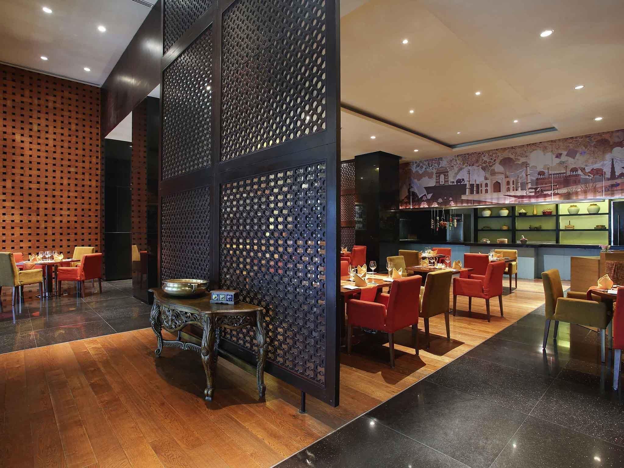 A restaurant with a modern interior, featuring a central decorative partition, wooden flooring, and a variety of seating arrangements including tables and chairs.