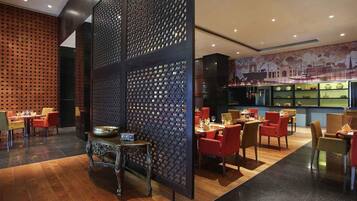 A restaurant with a modern interior, featuring a central decorative partition, wooden flooring, and a variety of seating arrangements including tables and chairs.