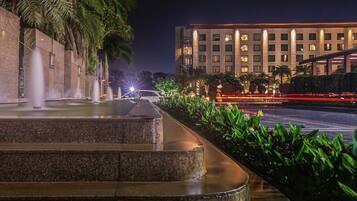 A nighttime view of a hotel with a water feature, palm trees, and a well-lit building facade.
