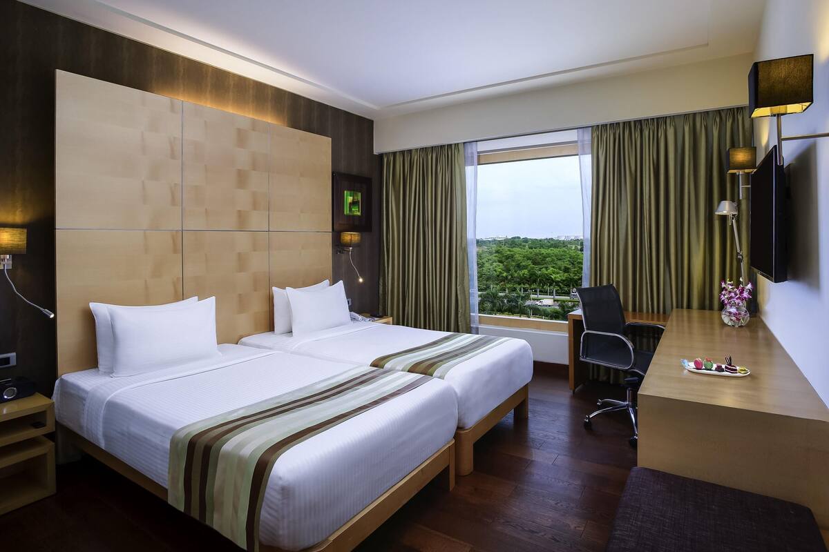 Une chambre d’hôtel avec un grand lit, un bureau et une vue sur la verdure environnante.