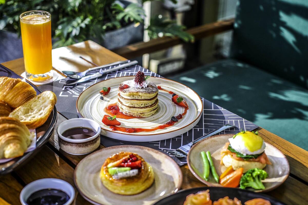 Une table avec des aliments pour le petit-déjeuner, notamment des crêpes, des croissants et un sandwich, ainsi qu'un verre de jus d'orange.