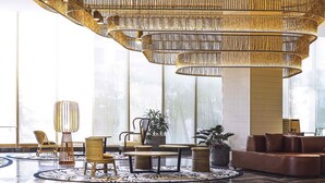 Un lobby amplio con techo alto, ventanas grandes y un área de estar central con una mesa redonda y sillas.