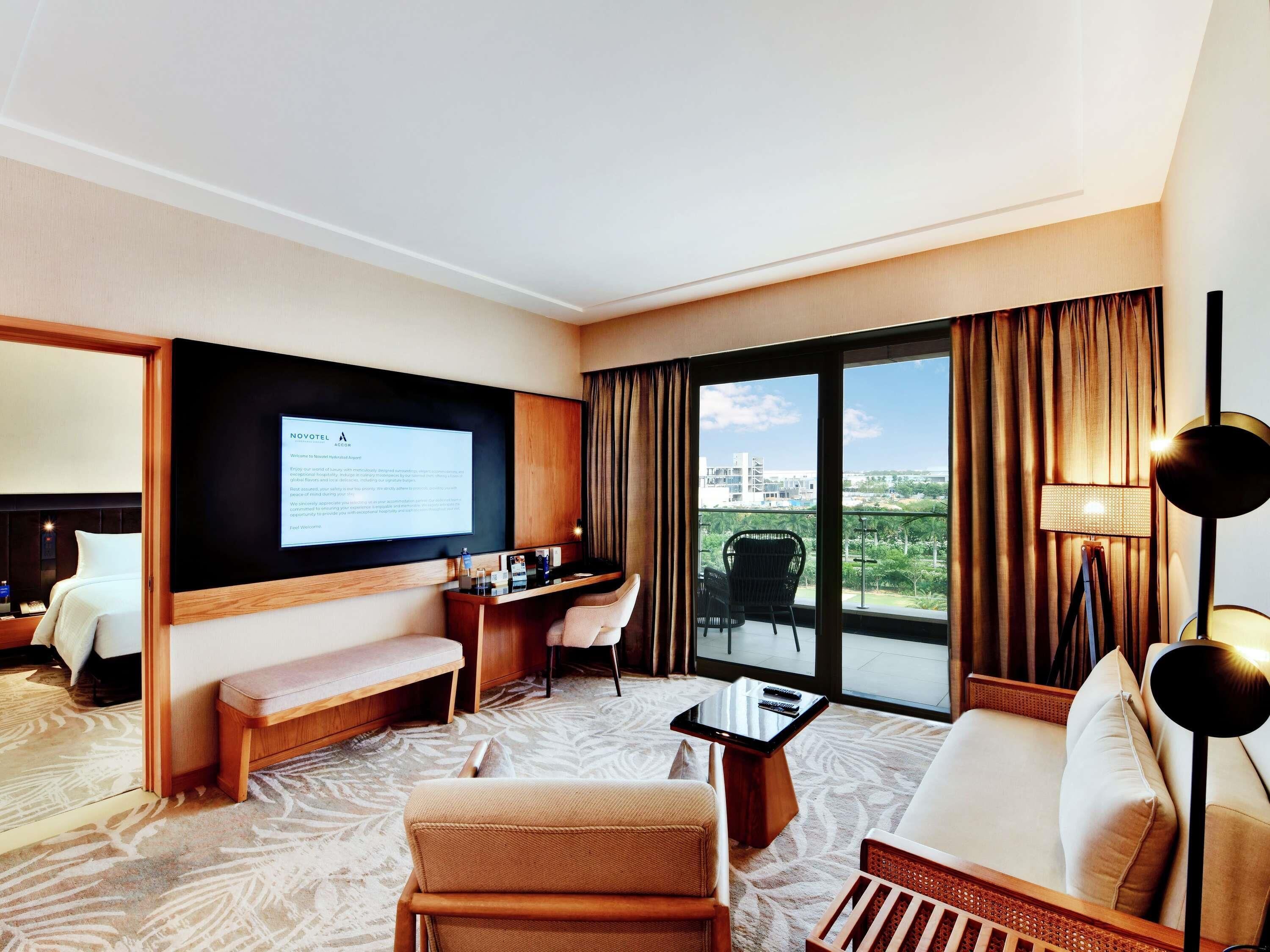 A hotel room with a bed, a desk, a sofa, a coffee table, and a large window with curtains.