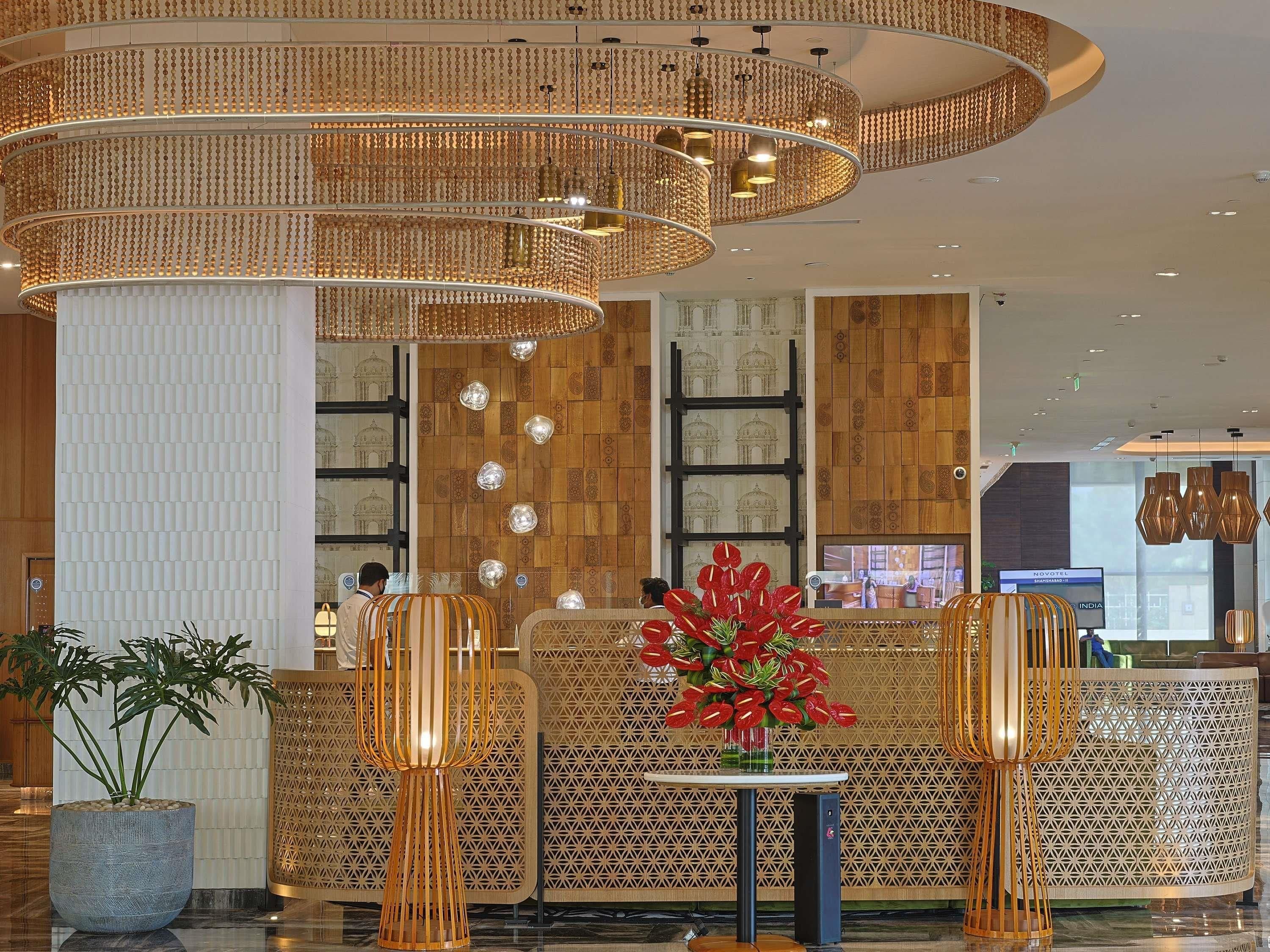A hotel lobby with a reception desk, patterned walls, and a modern chandelier.
