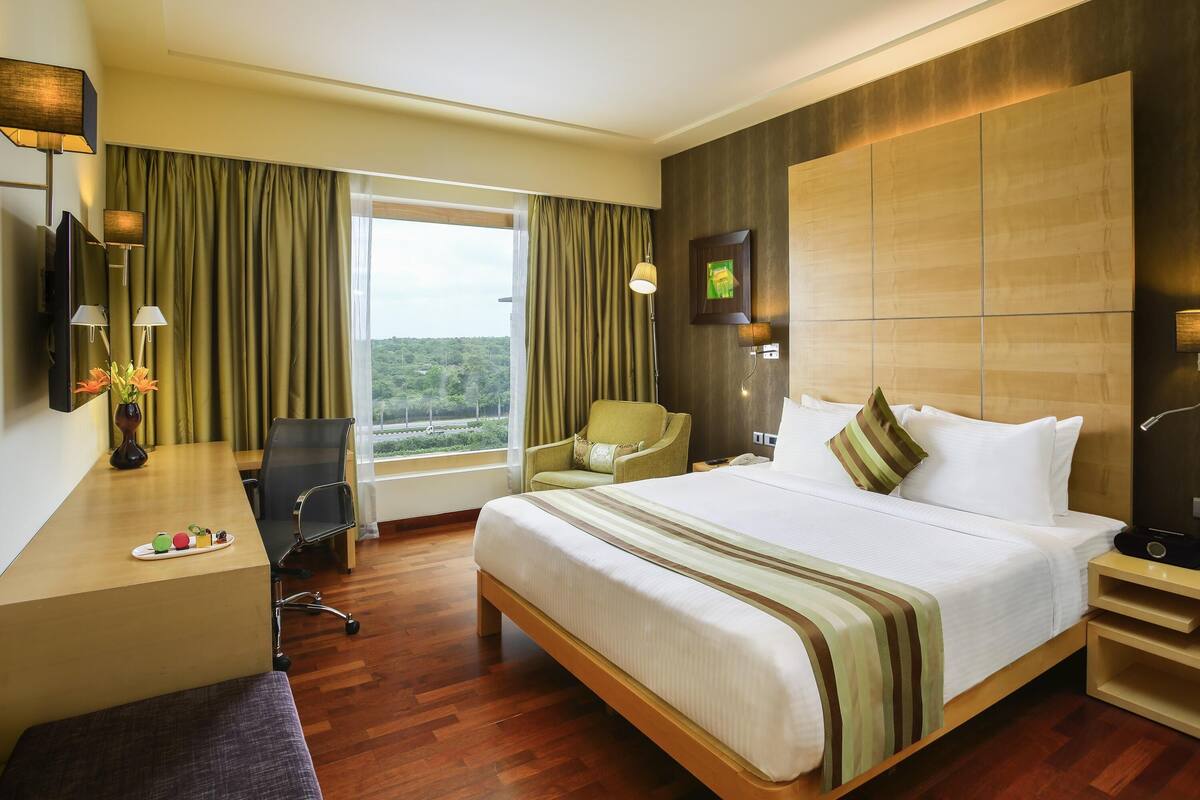 Une chambre d’hôtel avec un lit, un bureau, une chaise et une vue sur la verdure.