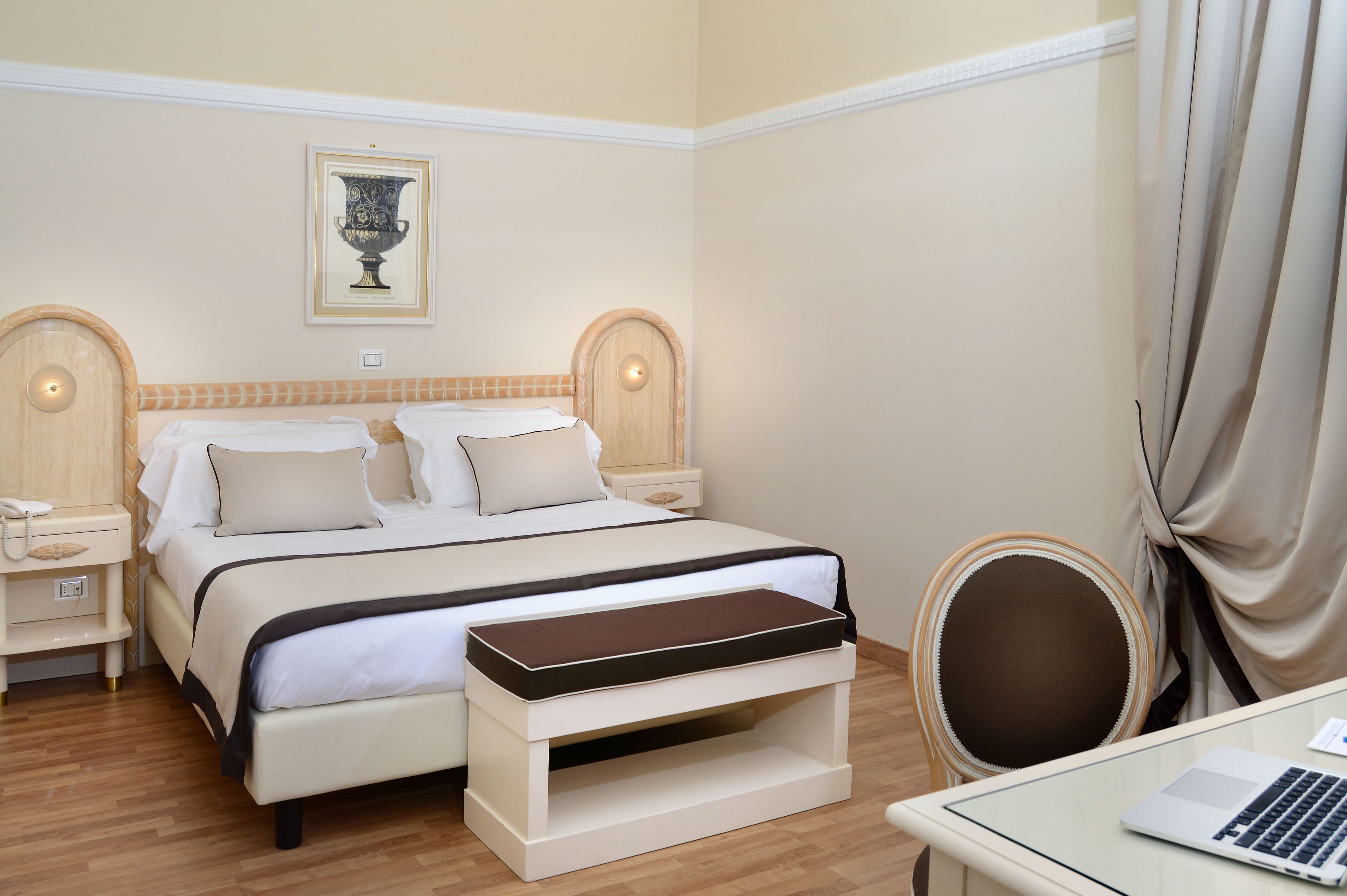 A hotel room with a bed, bedside tables, a desk with a laptop, and a chair.