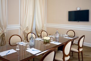 Un salón de conferencias con una larga mesa, sillas, un televisor montado en la pared y un centro de mesa floral.