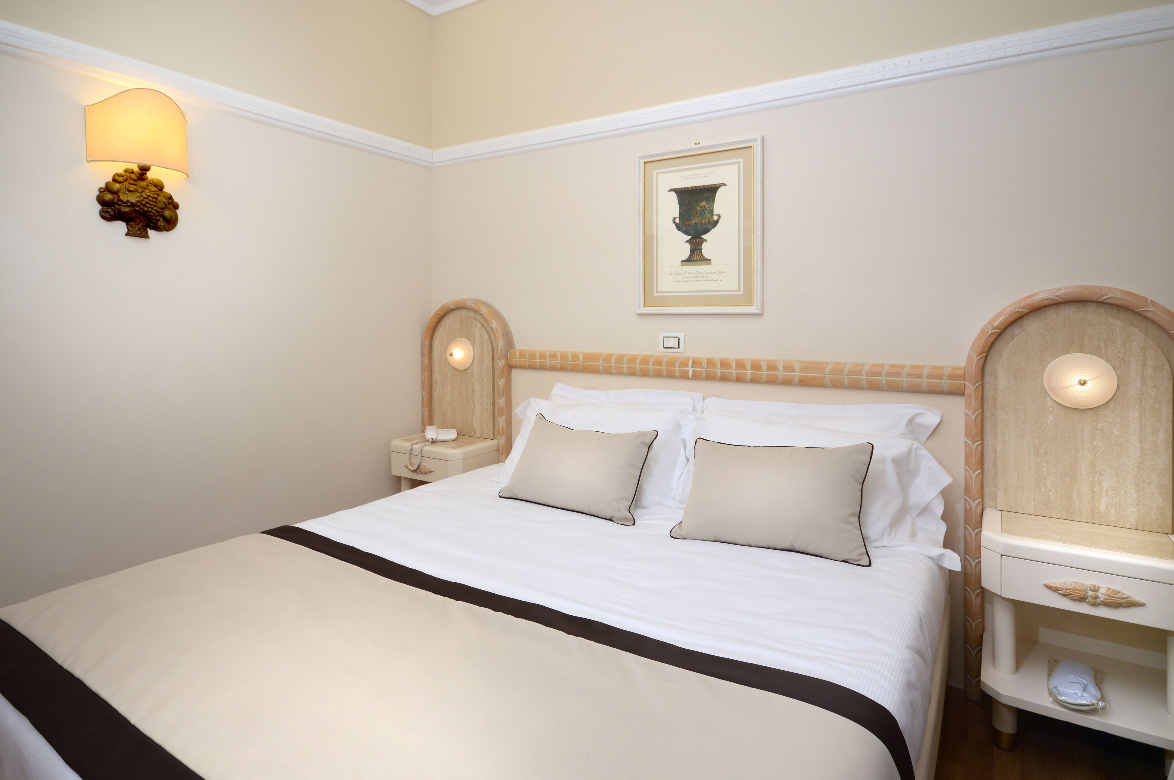 A neatly made bed with two pillows, a bedside table with a lamp, and a framed picture on the wall.