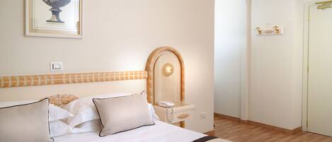 A hotel room with a bed, a bedside table with a phone, a mirror, and a framed picture on the wall.