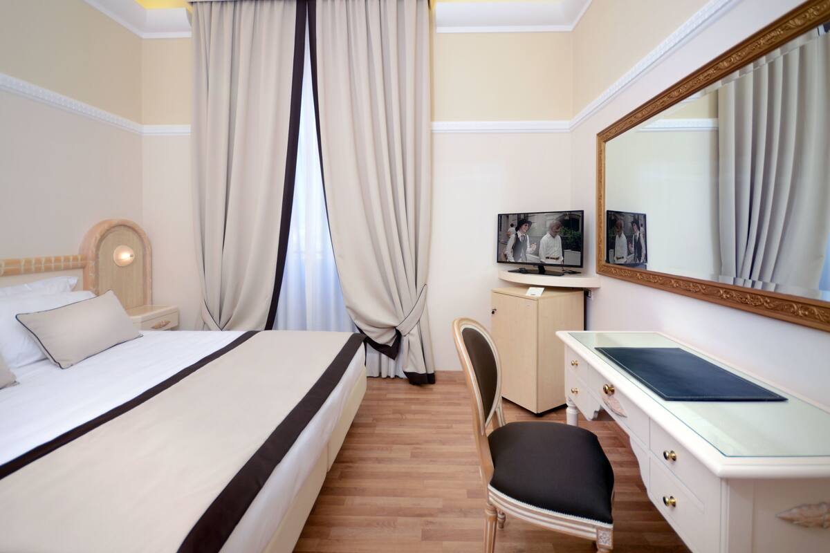 Ein Hotelzimmer mit einem großen Bett, einem Schreibtisch inklusive Spiegel, einem Fernseher und einem Sessel.