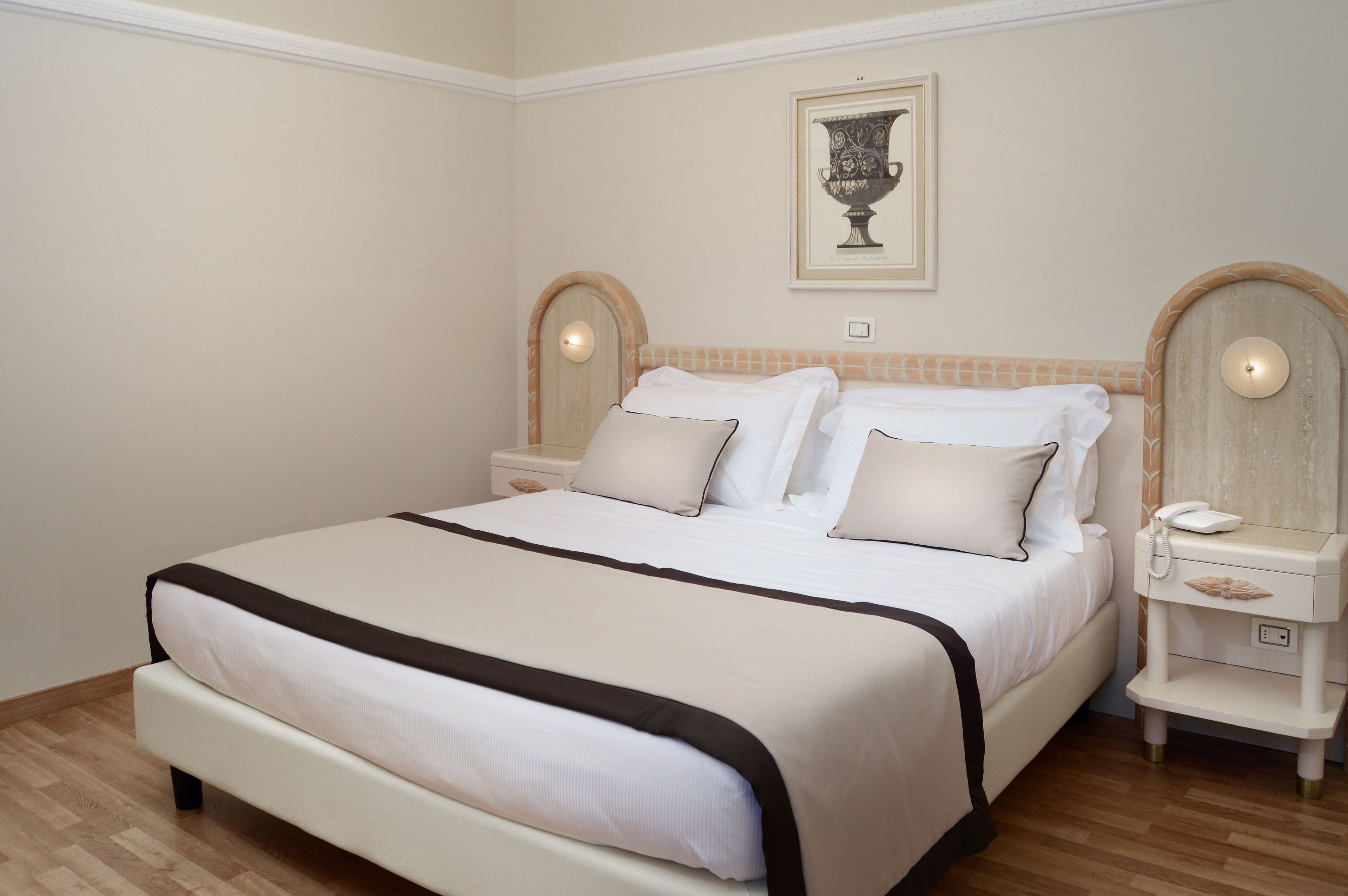 A neatly made bed with white linens and a black accent, a bedside table with a lamp, and a framed artwork on the wall.