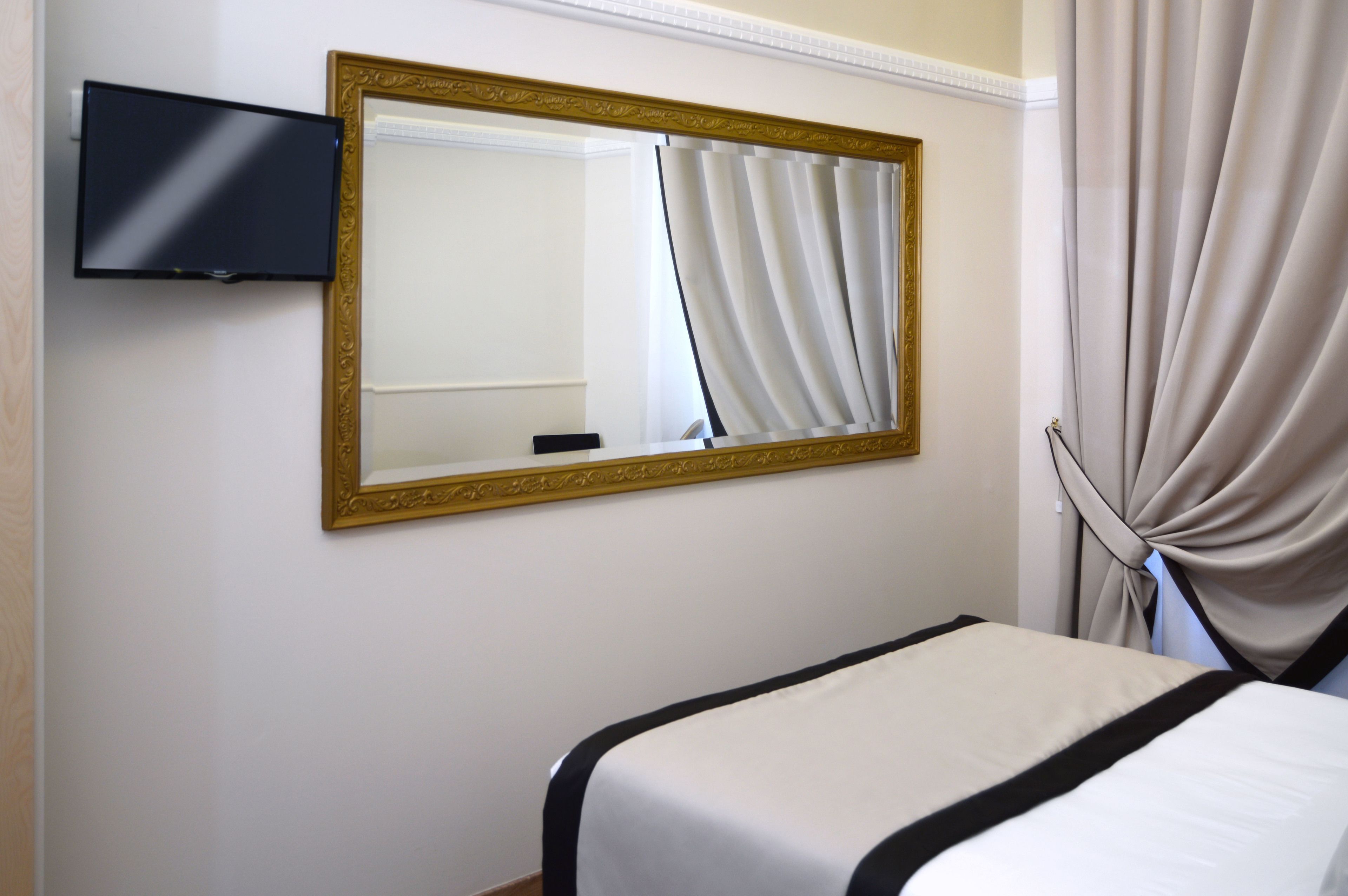 Una camera d'albergo con un letto, una televisione a parete e un grande specchio con cornice dorata.