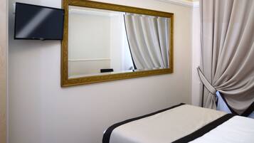 Una camera d'albergo con un letto, una televisione a parete e un grande specchio con cornice dorata.