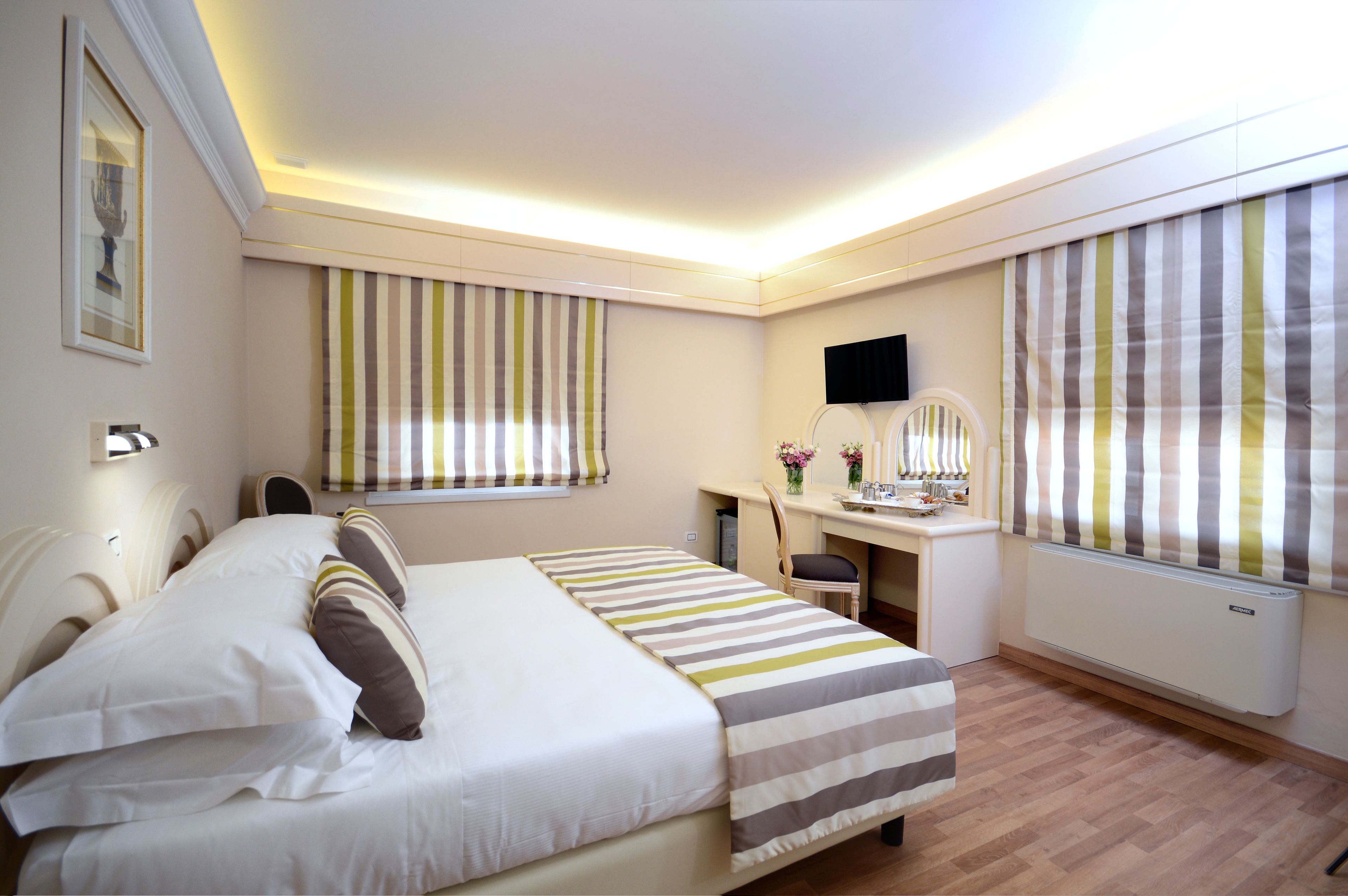 A hotel room with a bed, desk, chair, and large windows with striped curtains.