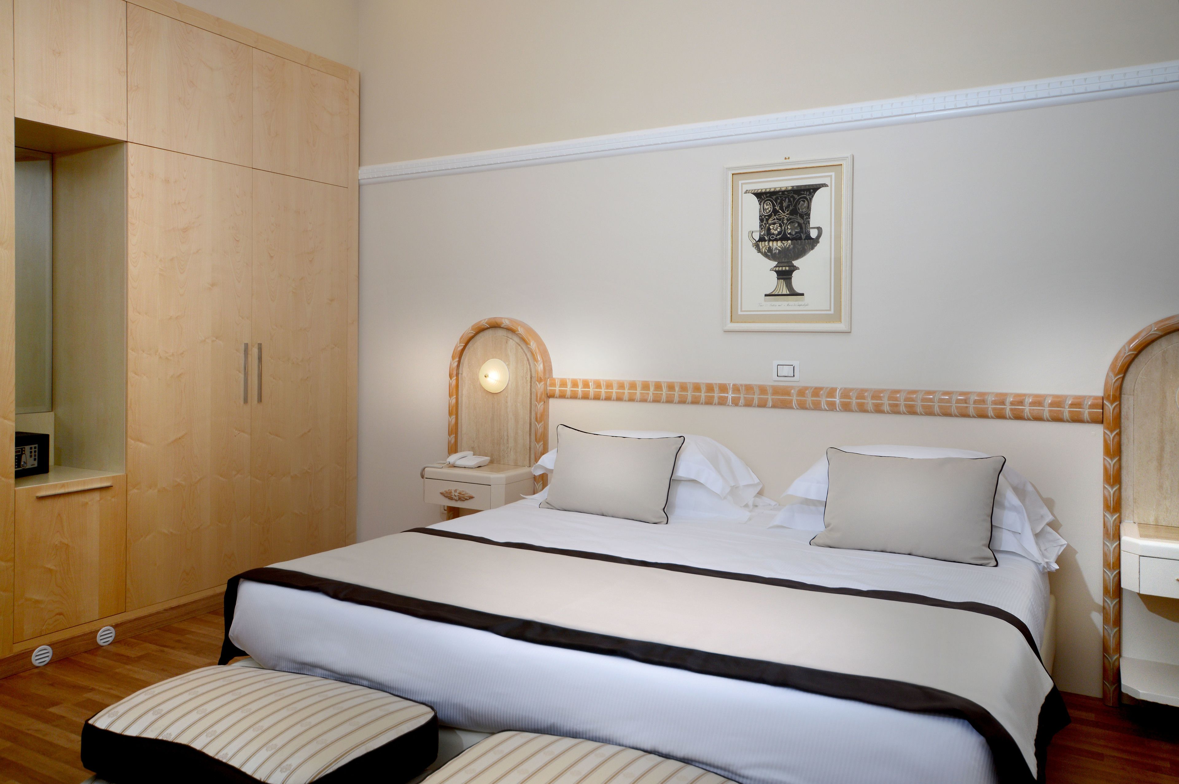 Habitación de hotel con una cama grande, un armario de madera, mesitas de noche y una obra de arte enmarcada en la pared.