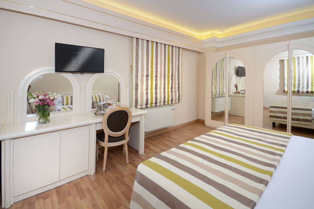 Ein Hotelzimmer mit Bett, Schreibtisch, Stuhl, Fernseher und Spiegel.