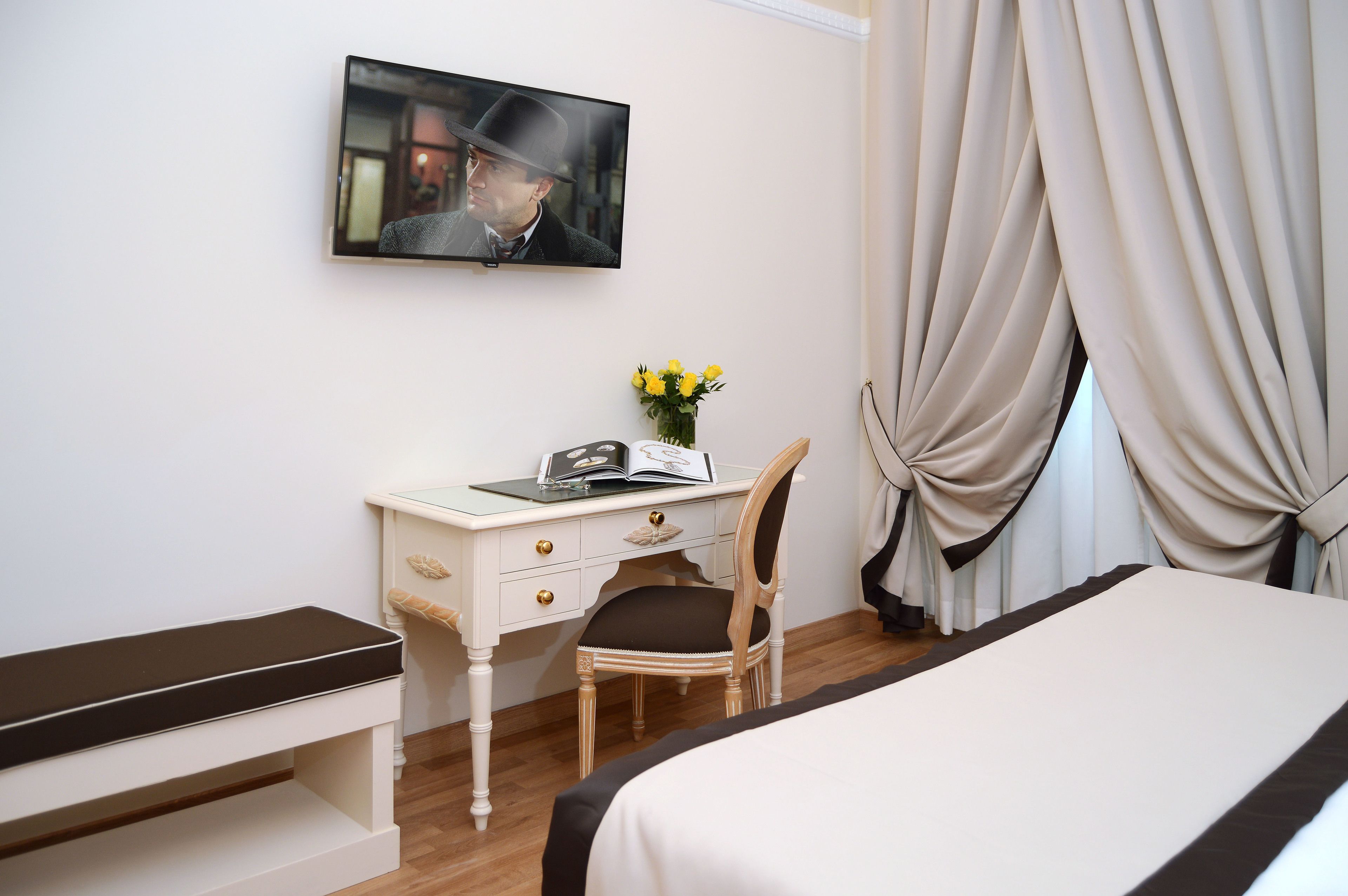 Una habitación de hotel con cama, escritorio con silla, televisor en la pared y cortinas.