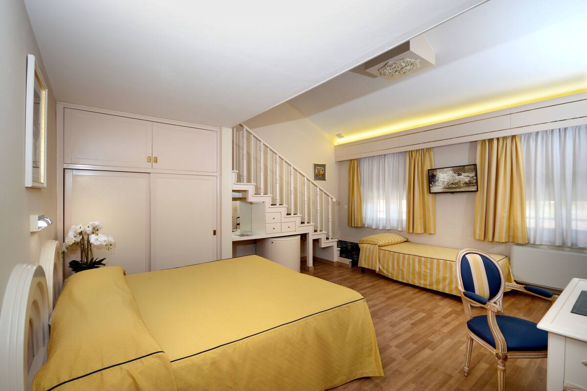 Ein Hotelzimmer mit einem Bett, einem Schreibtisch, einem Stuhl, einer Treppe und einem Fenster mit Vorhängen.