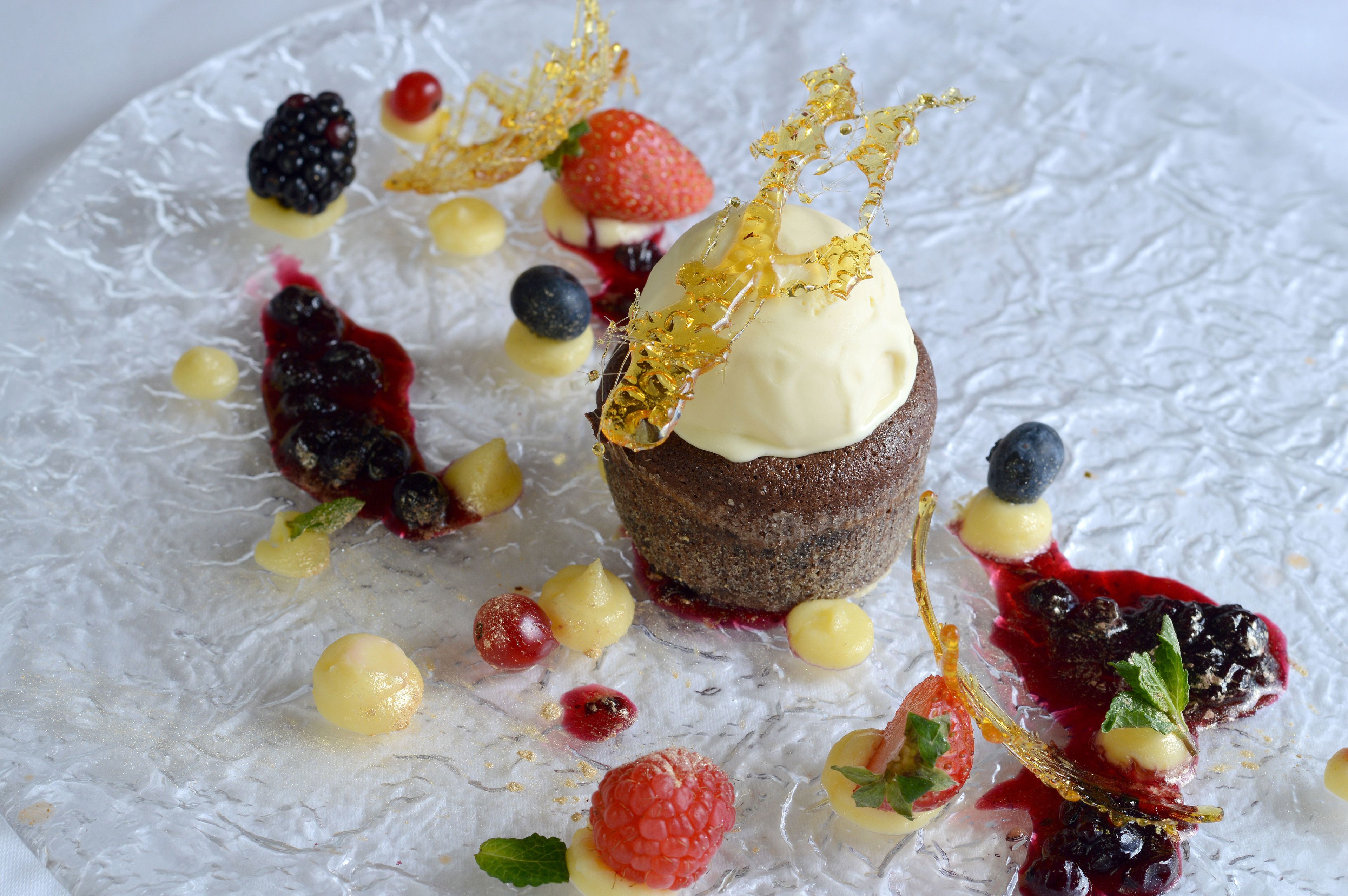 A dessert with ice cream and berries on a textured plate.
