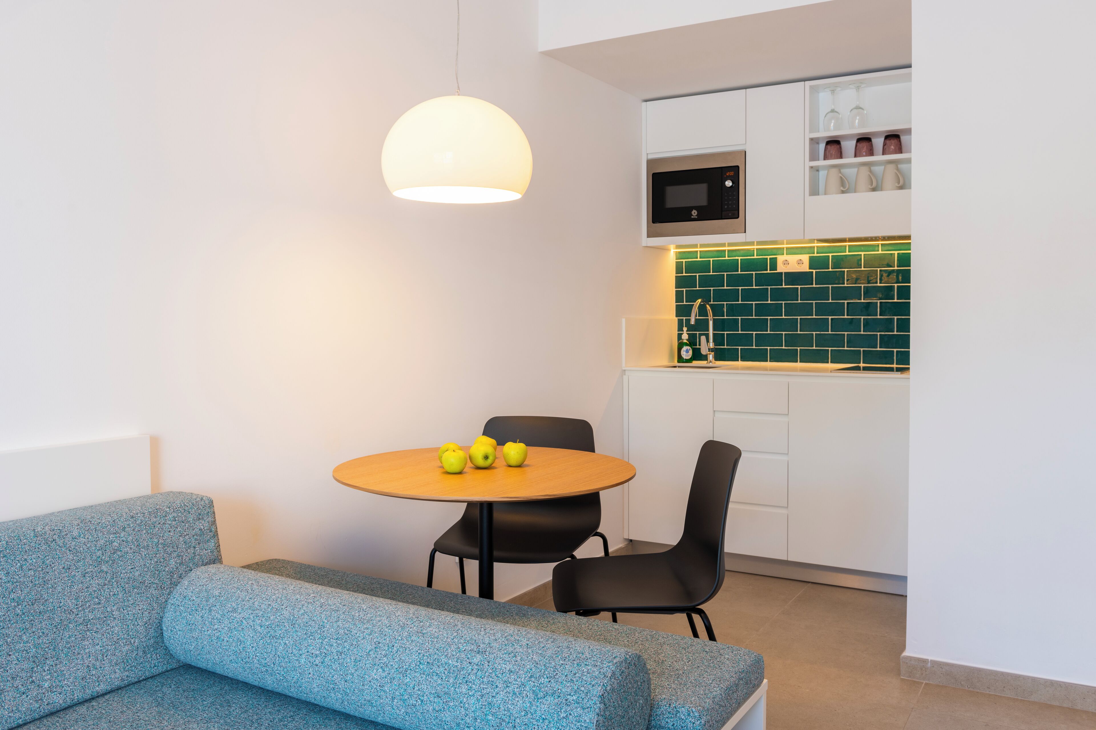 A compact living space with a kitchenette, a dining area with a round table and chairs, and a sofa.