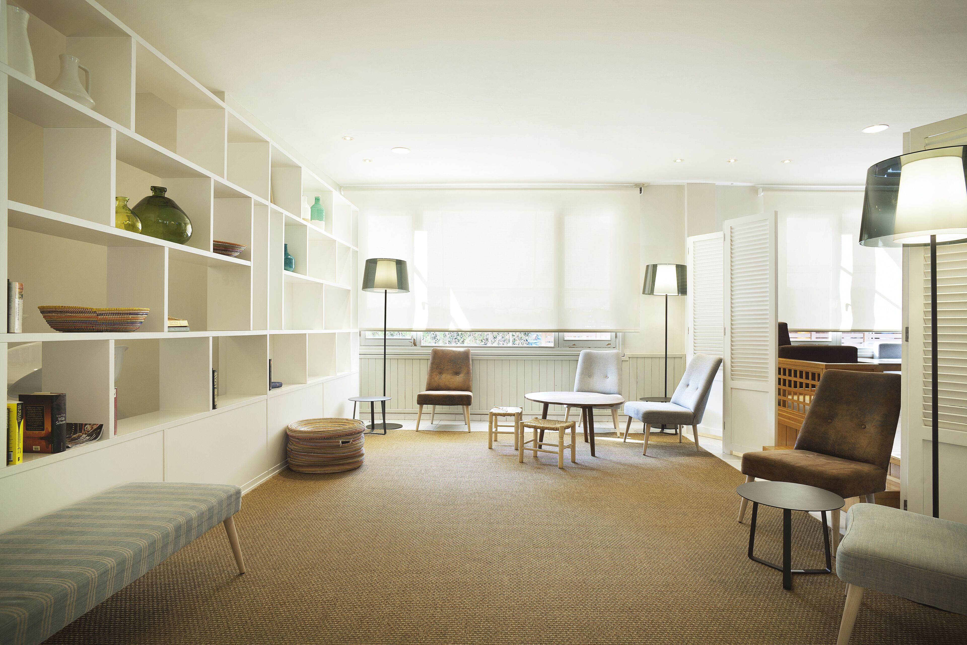Una habitación luminosa y amplia con una gran estantería, una zona de estar cómoda con sillas y una pequeña mesa, y vistas a través de una ventana.