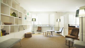 Una habitación luminosa y amplia con una gran estantería, una zona de estar cómoda con sillas y una pequeña mesa, y vistas a través de una ventana.